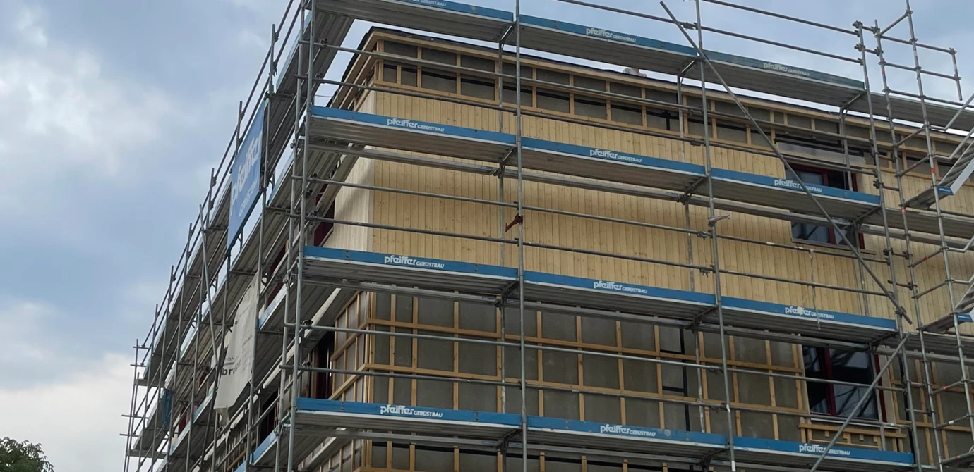 Holz auf Holz: Zwei Zimmerer von Sutter Holzbau beim Stellen des Firstbaums für den Neubau in der Neubaugasse, Lauterach. Darunter ist die Holzfassade sehr gut zu erkennen, die aktuell montiert wird.

